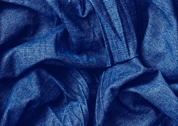 Detailní klasická modrá makro textura z modré džíny materiálu tkaniny nebo oblečení. Toned trendy 2020 rok barevné pozadí s vráskami a záhyby. Tmavě modrá monochromatická pozadí tapety. — Stock fotografie