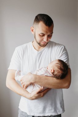 Genç beyaz bir baba yeni doğmuş bebeği sakinleştirmeye çalışıyor. Erkek anne.