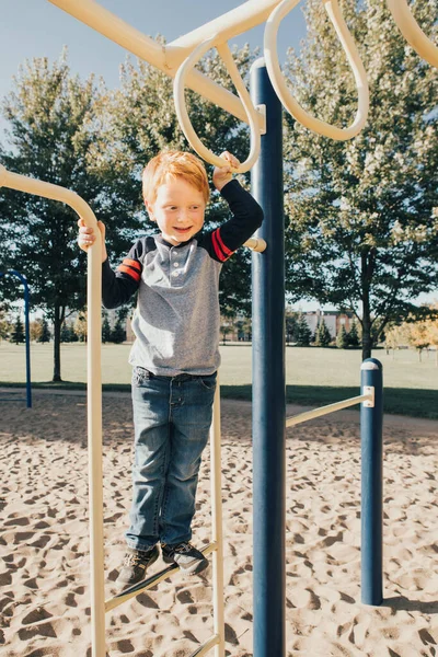 Jovem de cabelos vermelhos caucasiano menino pendurado em barras de macaco no parque em — Fotografia de Stock