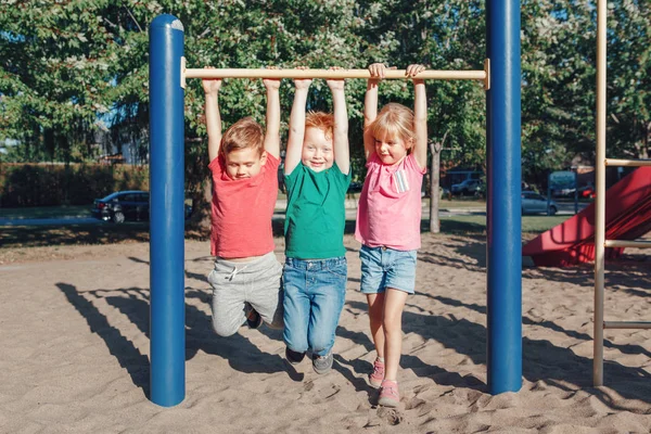 Three funny Caucasian friends hanging on pull-up bars in park on — стокове фото