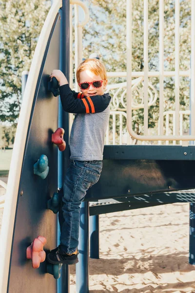 Boldog mosolygós kis óvodás fiú napszemüvegben sziklát mászik — Stock Fotó