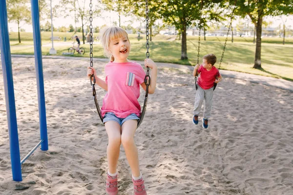 Szczęśliwy uśmiechnięty mały przedszkolak dziewczyna i chłopak przyjaciele swinging na — Zdjęcie stockowe
