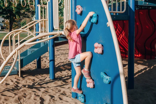 Little preschool girl climbing rock wall at playground outside o — 스톡 사진