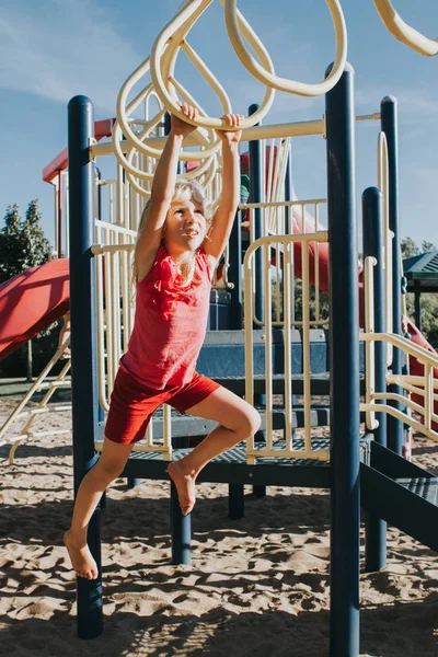 Joven chica rubia caucásica colgando en barras de mono en el parque en pl — Foto de Stock