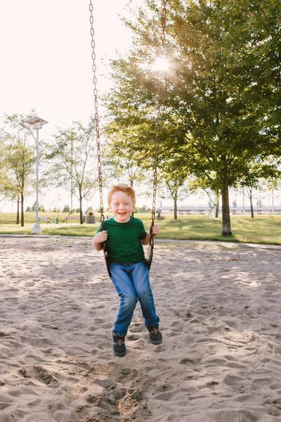 Feliz sorrindo menino pré-escolar balançando em swingsat playgrou — Fotografia de Stock