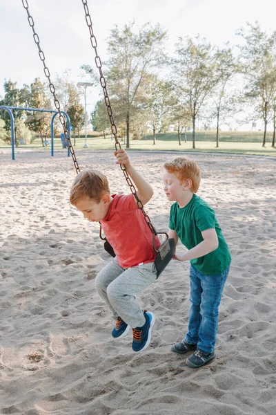 Щасливі усміхнені маленькі хлопчики дошкільного віку друзі гойдаються на гойдалках — стокове фото