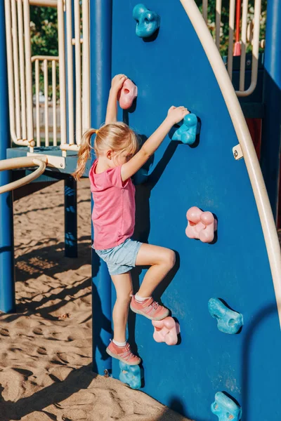 Pequena menina pré-escolar escalando parede de rocha no playground fora o — Fotografia de Stock