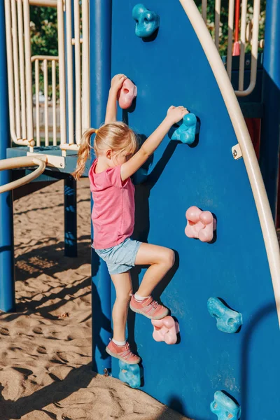 Kleine kleuter meisje klimmen rots muur op speeltuin buiten o — Stockfoto