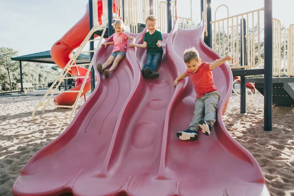 Actif heureux caucasien enfants glissant sur aire de jeux cour d'école — Photo