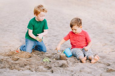 Two Caucasian children sitting in sandbox playing with beach toys. Little boys friends having fun together on playground. Summer outdoor activity for kids. Leisure time lifestyle childhood.
