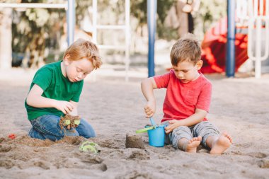 Two Caucasian children sitting in sandbox playing with beach toys. Little boys friends having fun together on playground. Summer outdoor activity for kids. Leisure time lifestyle childhood.
