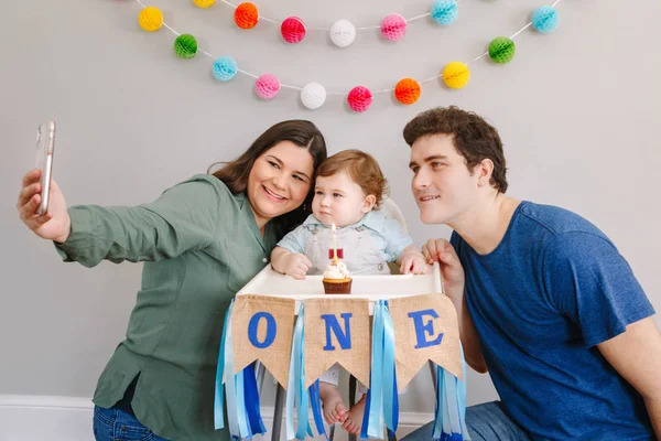 Ibu ayah mengambil selfie dengan anak balita. Keluarga Kaukasia dengan bayi laki-laki merayakan ulang tahun pertamanya di rumah. Cupcake dessert dengan satu lilin. Selamat ulang tahun konsep gaya hidup. — Stok Foto