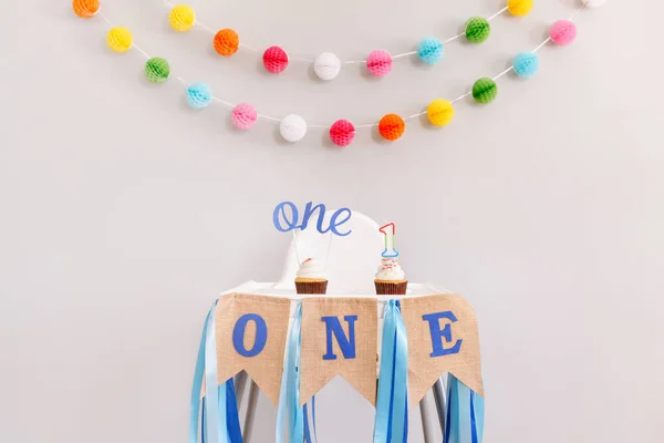 Festive background decoration for birthday celebration. Letters text one and one candle in small cupcakes for baby child birthday. Garland decoration on background. Cake smash first year. — 스톡 사진