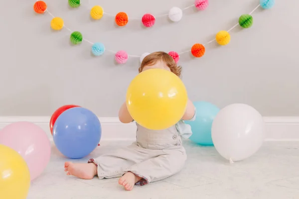 Αστείο καυκάσιο αγοράκι που γιορτάζει τα πρώτα του γενέθλια. Ενθουσιασμένο παιδί παιδάκι που παίζει με πολύχρωμα μπαλόνια. Γιορτή της εκδήλωσης ή πάρτι σε εσωτερικούς χώρους στο σπίτι. Χαρούμενα γενέθλια έννοια τρόπο ζωής. — Φωτογραφία Αρχείου