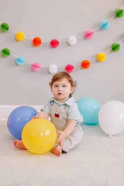 Funny Caucasian baby boy celebrating his first birthday. Excited child kid toddler playing with colorful balloons. Celebration of event or party indoors at home. Happy birthday lifestyle concept. — 스톡 사진