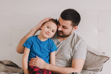 Genç, beyaz bir baba oğluyla konuşuyor. Erkek ebeveyn, evde, yatak odasında çocuğuyla sarılıyor. Otantik yaşam tarzı. Samimi bir an. Babalar Günün kutlu olsun.. 