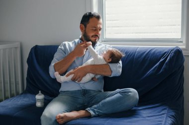 Gururlu beyaz bir baba ve yeni doğmuş bir kız bebek. Anne ve babası, sallanan kız evlat oğlunu ellerinde tutuyorlar. Otantik yaşam tarzı mutlu ebeveynlik anı. Bekar baba aile hayatı..