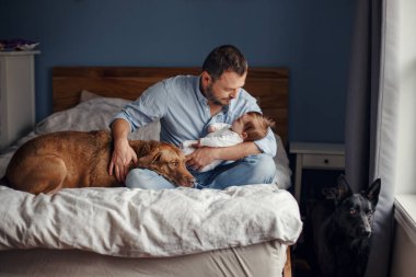 Orta yaşlı beyaz bir baba ve uyuyan yeni doğmuş bir kız bebek. Anne ve baba, sallanan kız evlat oğlunu ellerinde tutuyor. Otantik bir ebeveyn olma anı. Bekar baba aile hayatı..