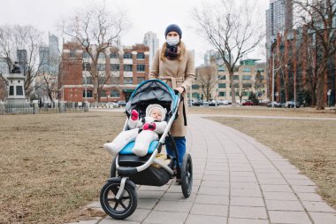 Cerrahi maske takan beyaz bir anne Toronto 'da bebekle dışarıda yürüyor. Yeni Çin atipik zatürree COVID-19 salgın virüs hastalığına karşı koruyucu yüz maskesi önlemi.
