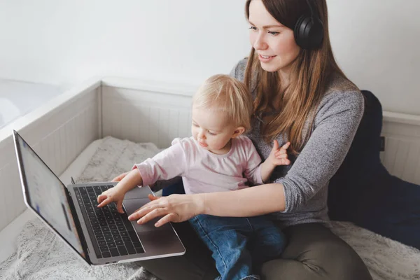 若い白人の母親ブロガーと赤ちゃんは自宅からノートパソコンで働いています 子供の幼児を持つフリーランスの女性学生の職場 家にいるシングルマザーオンライン仕事でお金を稼ぐ — ストック写真