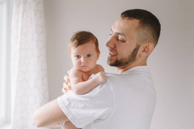 Yeni doğmuş bebeği tutan mutlu beyaz bir baba. Erkek sakallı adam, ebeveyn, sallanan küçük kız oğlu ellerinde. Otantik yaşam tarzı samimi anı. Genç baba aile hayatı konsepti.