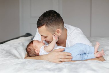 Beyaz bir baba yeni doğmuş bir bebekle yatak odasında yatıyor. Erkek ebeveyn kucaklaşması, kız evlat kucaklaması. Otantik yaşam tarzı samimi anı. Gururlu genç baba. Aile Babaları Günü.