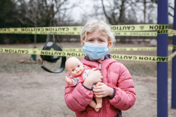 閉じた遊び場の屋外で赤ちゃんのおもちゃと顔のマスクで悲しい白人の女の子 子供たちはトロントカナダで黄色の警戒テープでロックされている地域を再生します コロナウイルス社会的距離隔離 — ストック写真