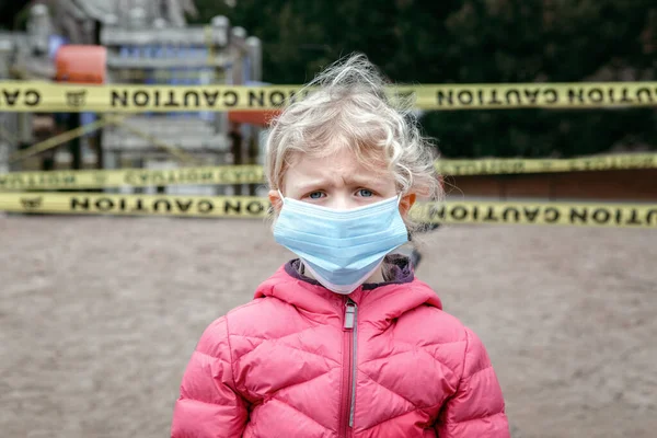 閉じた遊び場の屋外で顔のマスクに悲しい白人の少女の肖像画 子供たちはトロントカナダで黄色の警戒テープでロックされている地域を再生します コロナウイルス社会的距離隔離 — ストック写真