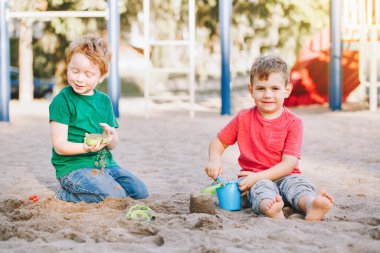Two Caucasian children sitting in sandbox playing with beach toys. Little boys friends having fun together on playground. Summer outdoor activity for kids. Leisure time lifestyle childhood.