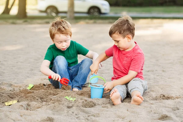 Two Caucasian children sitting in sandbox playing with beach toys. Little boys friends having fun together on playground. Summer outdoor activity for kids. Leisure time lifestyle childhood.
