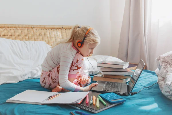 Caucasian girl child sitting in bed and learning online on laptop Internet. Virtual class lesson school on video chat during self isolation quarantine at home. Distant remote video education class.