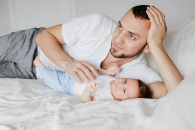 Yeni doğmuş bir bebekle evde yatan Kafkasyalı mutlu bir baba. Erkek ebeveyn kucağında kız evlat. Otantik yaşam tarzı samimi anı. Gururlu genç baba. Aile Babaları Günü.