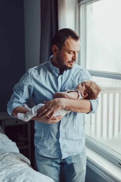 Middle age Caucasian father trying to calm down newborn baby. Man parent holding rocking child on his hands. Authentic lifestyle family moment. Single dad home life concept. Fathers Day.