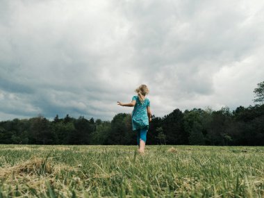 Meadow 'da koşan tatlı küçük kız. Çizme giymiş çocuk bacakları. Özgürlük masumiyeti ve ergenlik kavramı. Çocuklar için yaz eğlencesi açık hava aktivitesi. Arkadan bak. Düşük açı görünümü. 