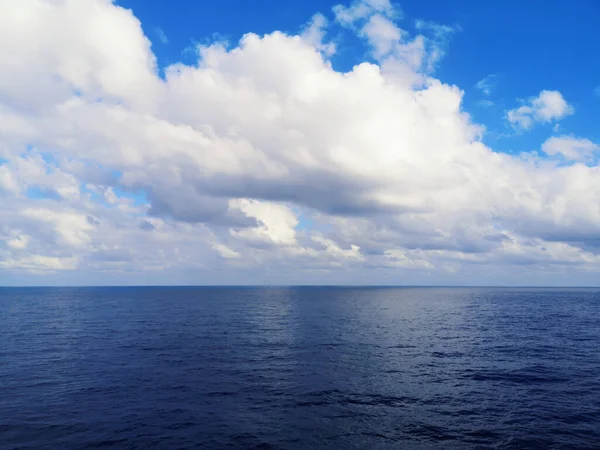 Gölde, okyanusta ya da denizde güzel bir manzara. Derin mavi su ve beyaz bulutlu ufukta inanılmaz bir manzara. Bulutlardan gelen güneş ışığı. Doğal ekolojik çevre geçmişi.