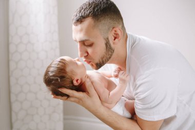 Yeni doğmuş bebeği öpen mutlu beyaz bir baba. Baba-baba, sallanan kız çocuğunu ellerinde tutuyor. Otantik yaşam tarzı samimi aile anı. Babalar Günü tatili.