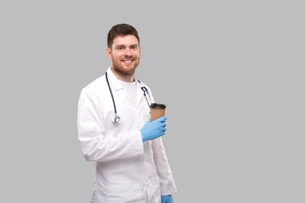 Doctor Holding Coffe Vidd el a kupát viselő kesztyű és mosolygós izolált — Stock Fotó