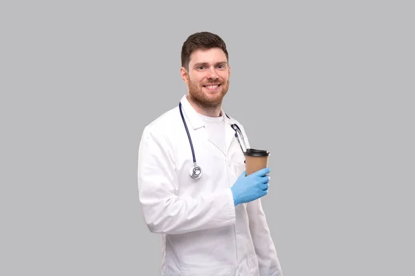 Doctor Holding Coffe tirar copo vestindo luvas e sorrindo isolado — Fotografia de Stock