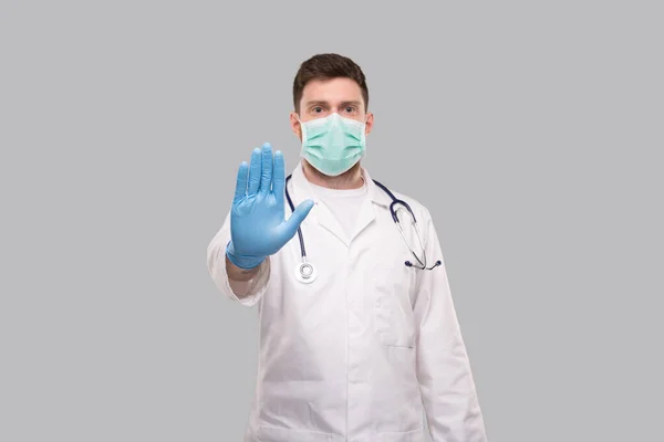 Man läkare visar stopp tecken. Läkare bär medicinsk mask och handskar. — Stockfoto