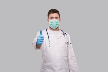 Erkek Doktor Başparmağını kaldırdı Tıbbi maske ve eldiven takıyor.