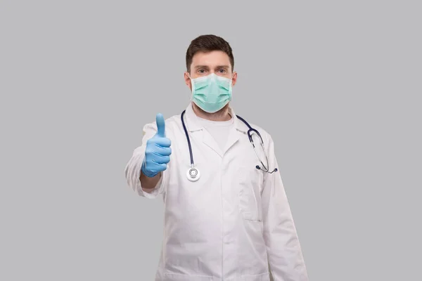 Männlicher Arzt zeigt Daumen hoch mit medizinischer Maske und Handschuhen. — Stockfoto