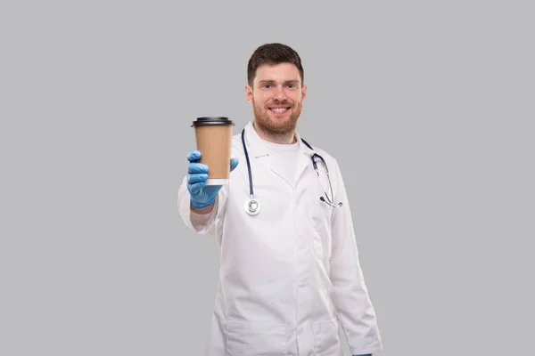 Dottore mostrando caffè di andare tazza indossando guanti e sorridente isolato — Foto Stock