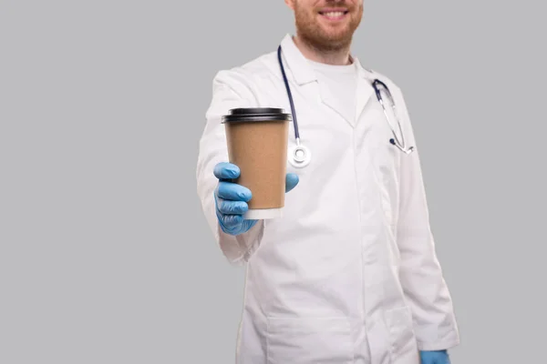 Doctor Mostrando Café Para Ir Copa Usando Guantes y Sonriendo Aislado. Café Take Away Cup Close Up —  Fotos de Stock