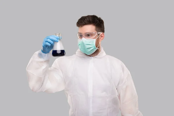 Male Laboratory Worker in Chemical Suit, Wearing Medical Mask and Glasses Watching Flask with Colorfull Liquid. Science, Medical, Virus Concept. Doctor