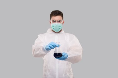 Kimyasal Takım Elbiseli Erkek Laboratuvar İşçisi, Tıbbi Maske Giyiyor ve Gözlüklü Renkli Sıvı Şişesi Gösteriyor. Bilim, Tıp, Virüs Konsepti. Kimyasallar