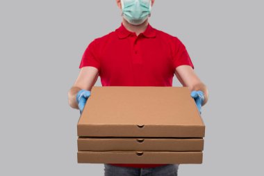 Ellerinde üç pizza kutusu olan tıbbi maske ve eldiven takan teslimatçı. Kırmızı Tişörtlü Teslimatçı. Kapatın. İzole edilmiş