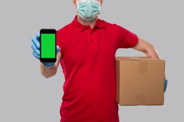 Teslimatçı, tıbbi maske takıyor ve Eldivenli, Kutulu Telefonu gösteriyor. Eve Teslimat. Sipariş Çevrimiçi Teknoloji. Yeşil Ekran Kapat 'ı ara. İzole edilmiş