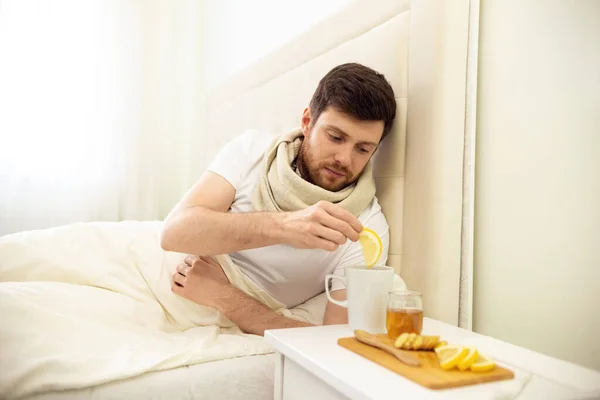 Sick Man in Bed Adding Lemon into Tee. Man Ill in Bed Self Healing. Self Treatment at Home. Man Drinking Hot Tea in Bed. — Stock Photo, Image