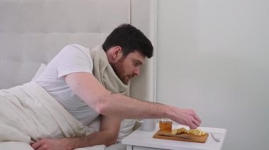 Yataktaki hasta adam Tee 'ye limon ekliyor. Hasta Adam, Yatak Kendini İyileştiriyor. Evde kendini tedavi etme. Yatakta Sıcak Çay İçen Adam