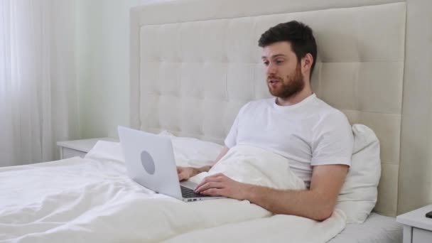 男人有视频呼叫床在笔记本电脑上。家庭视频呼叫。在家里从床上干活。在线工作。病床上的笔记本电脑视频通话 — 图库视频影像